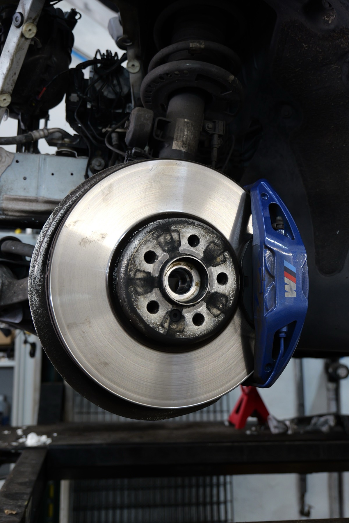 A front brake disc and blue M-sport caliper on a car in the workshop